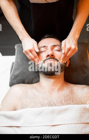 Bärtiger Mann, der eine Gesichtsmassage erhält, sich im Spa-Salon entspannt, Blick von oben Stockfoto