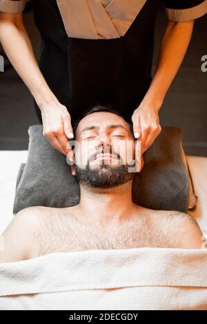Bärtiger Mann, der eine Gesichtsmassage erhält, sich im Spa-Salon entspannt, Blick von oben Stockfoto