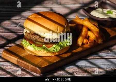 Nahaufnahme des hausgemachten Hamburgers mit Bier aus Rind, Zwiebeln, Tomaten, Salat, Käse und Gewürzen. Frische Burger auf rustikalem Holztisch Stockfoto