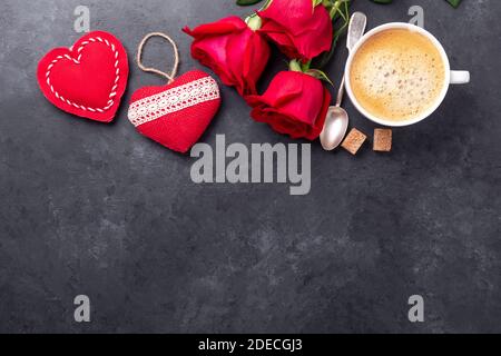Grußkarte zum Valentinstag. Kaffeetasse, rote Rosen und textile Herzen auf steinernem Hintergrund. Draufsicht - Bild Stockfoto