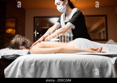 Professionelle weibliche Masseur in Gesichtsmaske tun Massage für einen Kunden im Spa Salon. Geschäft während des epidemischen Konzepts Stockfoto