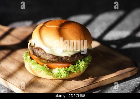 Nahaufnahme des hausgemachten Hamburgers mit Bier aus Rind, Zwiebeln, Tomaten, Salat, Käse und Gewürzen. Frische Burger auf rustikalem Holztisch Stockfoto