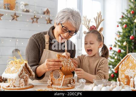 Frohe Weihnachten und frohe Feiertage. Familienzubereitung Urlaub Essen. Großmutter und Enkelin Kochen Lebkuchenhaus. Stockfoto