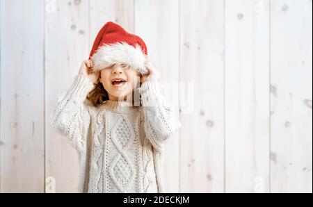 Glückliches kleines Mädchen mit Weihnachtsmann Hut auf weißem Holzhintergrund zu Weihnachten. Stockfoto