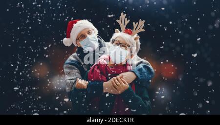 Frohe Weihnachten! Winterportrait des älteren Paares auf schneebedecktem dunklen Hintergrund. Menschen mit Gesichtsmasken. Stockfoto