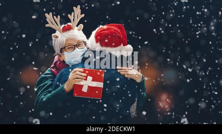 Frohe Weihnachten! Winterportrait des älteren Paares auf schneebedecktem dunklen Hintergrund. Menschen mit Gesichtsmasken. Stockfoto