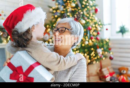 Frohe Weihnachten und schöne Feiertage! Fröhliche Oma und ihre niedliche Enkelin Mädchen tauschen Geschenke. Oma und kleines Kind Spaß in der Nähe von Baum ich Stockfoto