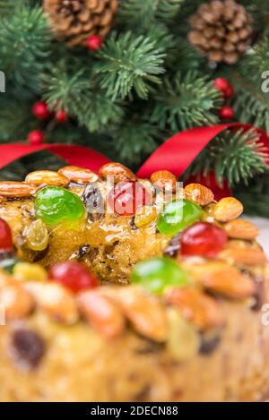 Glasierte runde hohle Weihnachtsfruitkuchen mit Mandeln und Glace Kirschen vor rotem Band, grünen Kiefernnadeln und Zapfen gekrönt Stockfoto