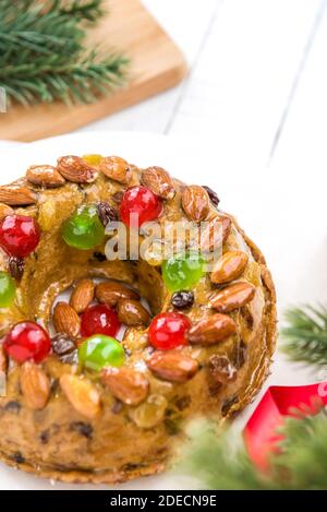 Glasierte runde hohle Weihnachtsfruitkuchen mit Mandeln und Glace gekrönt Kirschen auf weißem Teller mit grünen Kiefernnadeln und rot Bändchenverzierungen Stockfoto