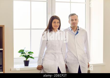 Porträt von zwei Ärzten, die am Fenster stehen und lächelnd auf die Kamera blicken. Stockfoto