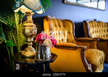 Nahaufnahme von roten und weißen Blüten in einem Metall Eimer auf kleinem Holztisch mit goldgelben Stühlen Der Hintergrund Stockfoto
