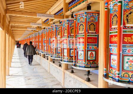 Xiahe, Provinz Gansu / China - 28. April 2017: Hölzerne Gebetsräder im Kloster Labrang. Mit Pilgern, die vorbei gehen und die Räder drehen. Stockfoto