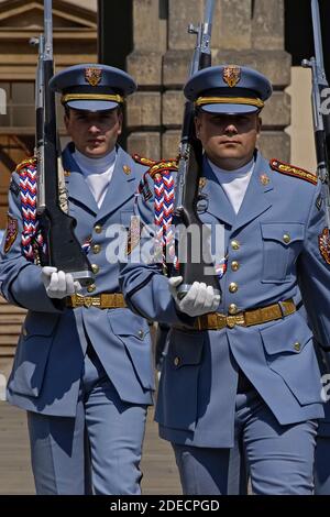 Zwei Wachposten der Prager Burgwache in ihren blassblauen Sommeruniformen marschieren mit geschulterten Gewehren mit Bajonetten, die während einer Wachwechsel-Zeremonie im ersten Burghof fixiert wurden, auf den Betrachter zu. Die Wachposten an den Toren der mittelalterlichen Burg wechseln zur vollen Stunde, und es gibt auch einen täglichen 12 Uhr mittags zeremoniellen Wachwechsel, einschließlich einer Fanfare und einer Flaggenzeremonie. Das Schloss ist der offizielle Sitz und das Büro des Präsidenten der Tschechischen Republik oder Tschechiens. Stockfoto