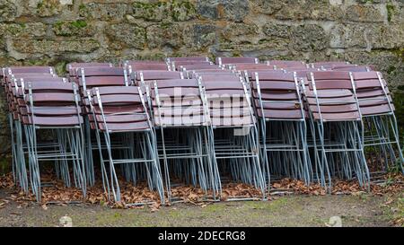 München, Bayern / Deutschland - 12. Nov 2020: Gefaltete Stühle lehnen sich an eine Steinwand. Alle Restaurants sind wegen der Covid-19-Sperre geschlossen. Stockfoto