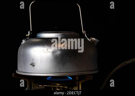 Alt schlug herauf Stahlkessel kochendes Wasser auf einem Campinggasherd mit einer blauen Flamme. Isoliert auf schwarzem Hintergrund. . Hochwertige Fotos Stockfoto