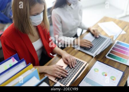 Zwei Frauen am Arbeitstisch in schützenden medizinischen Masken. Stockfoto