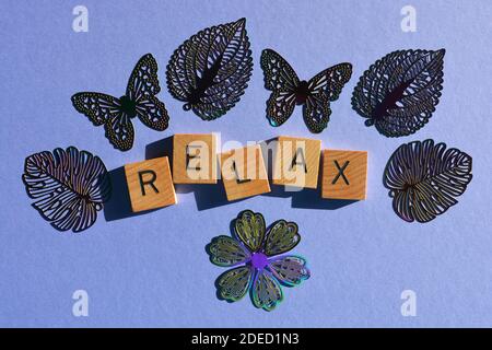 Entspannen Sie sich, Wort in Holzbuchstaben umgeben von Blumen-, Blatt- und Schmetterlingsmotiven Stockfoto