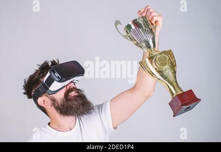 Feiere den Sieg. Spüren Sie den Sieg in Virtual Reality-Spiele. Sieg. Hipster virtuelle Gamer bekam Erfolg. Mann Gewinner virtuellen Wettbewerb. Mann bärtige Hipster vr Headset hält goldenen Kelch. Stockfoto