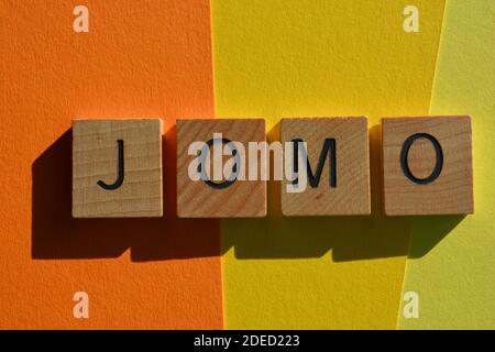 JOMO Akronym für Freude am Verfehlen, in hölzernen Buchstaben auf buntem Hintergrund isoliert Stockfoto