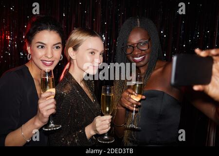 Porträt von drei eleganten jungen Frauen halten Champagner Gläser und lächeln während der Aufnahme Selfie Foto auf der Party, mit Blitz aufgenommen Stockfoto