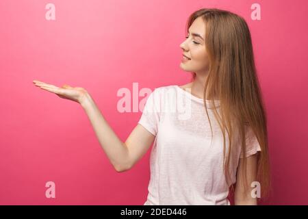 Nahaufnahme Porträt der glücklichen blonden Frau zeigt den Vorderfinger zur Seite, steht auf einem rosa Hintergrund, zeigt etwas in leeren Kopieplatz für adv Stockfoto