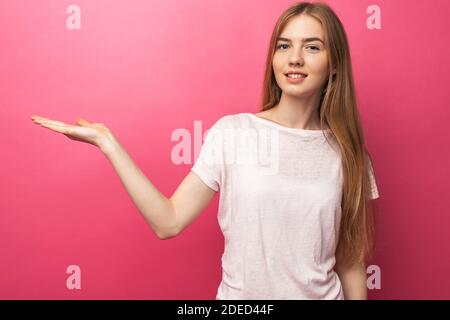 Nahaufnahme Porträt der glücklichen blonden Frau zeigt den Vorderfinger zur Seite, steht auf einem rosa Hintergrund, zeigt etwas in leeren Kopieplatz für adv Stockfoto