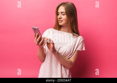 Portrait von fröhlichen schönen Mädchen beobachten das Telefon, SMS, isoliert auf rosa Hintergrund, Stockfoto