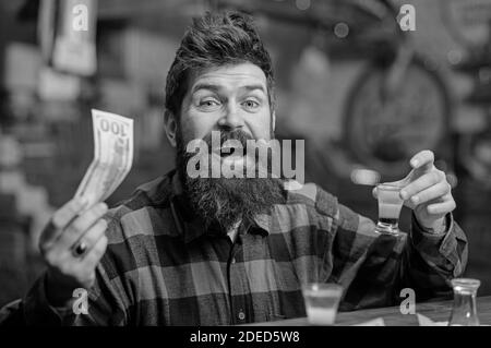 Kerl verbringen Freizeit in der Bar trinken Cocktail, entkokettes Hintergrund. Getränke kaufen Konzept. Hipster hält Geld, Bargeld, um mehr Alkohol zu kaufen. Mann mit fröhlichem Gesicht sitzt allein an der Theke. Stockfoto