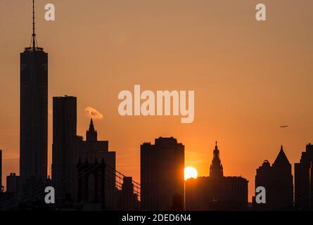 USA, New York City, Skyline von Manhattan, One World Trade Center ganz links. Sonnenuntergang und ein Flugzeug steigt. Der Blick vom Brooklyn Naval Yard. Stockfoto