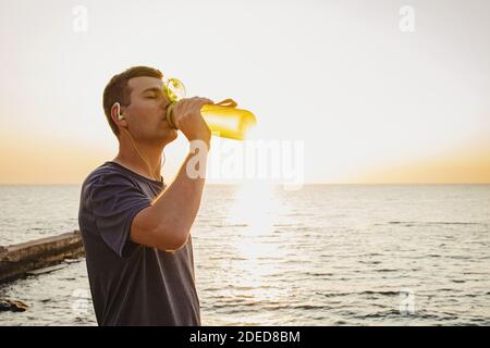 Mann Trinkwasser aus der Flasche nach dem Joggen in der Nähe Das Meer Stockfoto