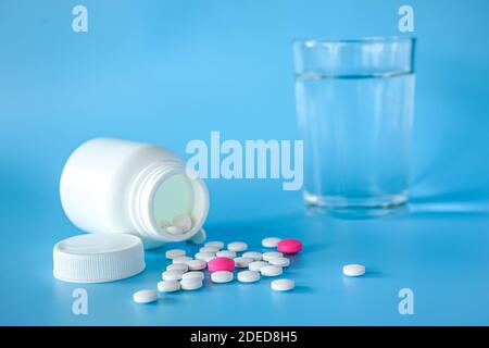 Nahaufnahme von Teblets Pillen mit Pillenflasche und ein Glas Wasser auf blauem Hintergrund Stockfoto