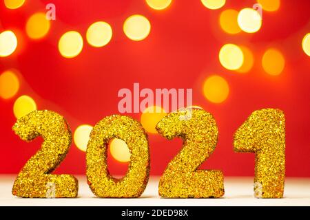 Goldene Glitzerzahlen 2021 mit Bokeh auf rotem Hintergrund. Frohe weihnachten und ein Frohes neues Jahr. Stockfoto