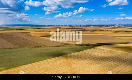 Blick über landwirtschaftliche Felder, kultivierte Parzellen in der Erntezeit, blauer Himmel mit weißen flauschigen Wolken ihre Schatten sind auf dem Boden. Stockfoto