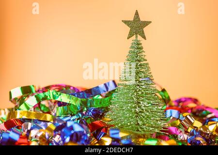 Kleine Spielzeug Tannenbaum und Folie Dekorationen auf beigem Hintergrund. Weihnachtskomposition mit Kopierraum, selektiver Fokus Stockfoto