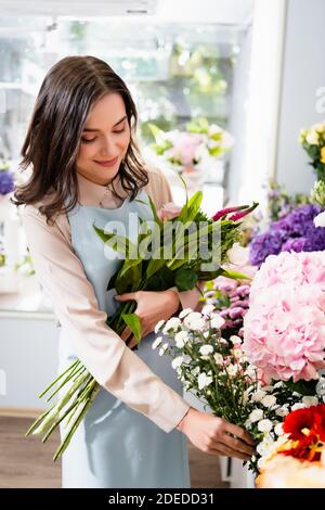 Lächelnd Floristen unter Zweig der Chrysantheme, während der Sammlung Strauß in der Nähe von Blumen mit auf verschwommenem Hintergrund Stockfoto