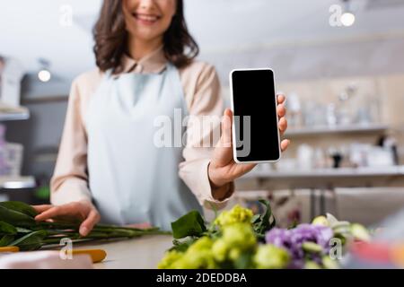 Zugeschnittene Ansicht des Floristen zeigt Smartphone mit leerem Bildschirm in der Nähe eustoma Blumen auf Schreibtisch auf verschwommenem Hintergrund Stockfoto
