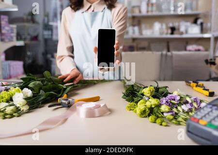 Zugeschnittene Ansicht des Floristen zeigt Smartphone mit leerem Bildschirm mit eustoma Blumen auf Schreibtisch auf verschwommenem Hintergrund Stockfoto
