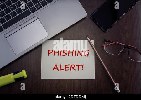 Phishing-Warnkarte. Draufsicht auf Bürotisch Desktop-Hintergrund mit Laptop, Telefon, Brille und Bleistift mit Karte mit Inschrift Phishing Alert. Stockfoto