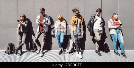 Multirassische Menschen mit Handy-Smartphone mit Gesichtsmaske bedeckt - Junge Freunde teilen Inhalte auf dem Smartphone - Neue Normalität Lifestyle-Konzept Stockfoto