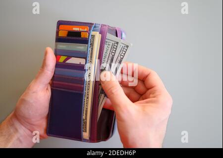 Herren Hände halten 100 Dollar Scheine und eine Brieftasche auf Ein grauer Hintergrund Stockfoto