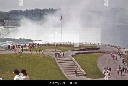 1970s Photo (1973) - Touristen im Park auf Goat Island Genießen Sie einen spektakulären Blick auf ''Horseshoe Falls'' die kanadische Hälfte Der Niagarafälle Stockfoto