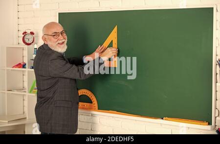 Tutor Mann in Brille zeichnen mit Dreieck auf Tafel. Zurück zur Schule. Welchen Winkel Sie suchen. Geometrische Formen. High School moderne Bildung. Senior man Lehrer verwenden Triagle beim Zeichnen. Stockfoto