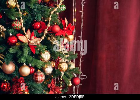 Goldene und rote Weihnachtsspielzeuge, Bälle, Girlanden auf einem Fichtenzweig auf dunkelrotem Hintergrund. Stockfoto