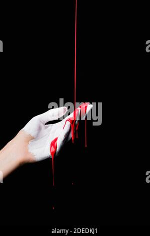 Teilansicht der weiß bemalten Hand mit roter tropfender Farbe Isoliert auf Schwarz Stockfoto
