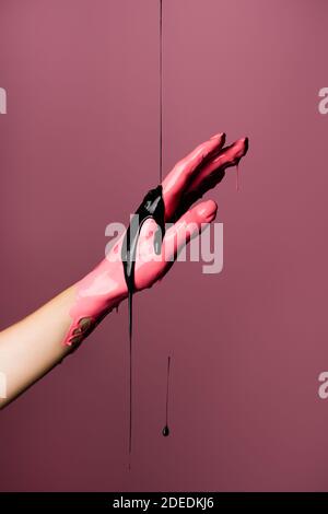 Teilansicht der Hand mit tropfender Farbe isoliert auf rosa Stockfoto