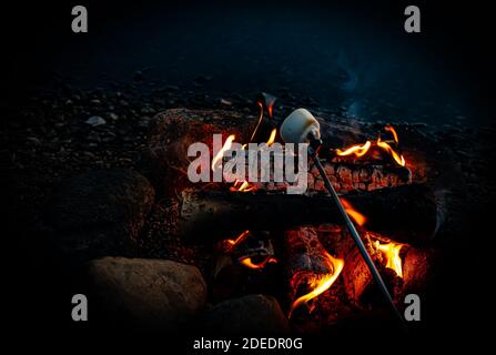 Marshmallow auf einem Stock, rösten über einem Lagerfeuer am See im Abendlicht. . Hochwertige Fotos Stockfoto