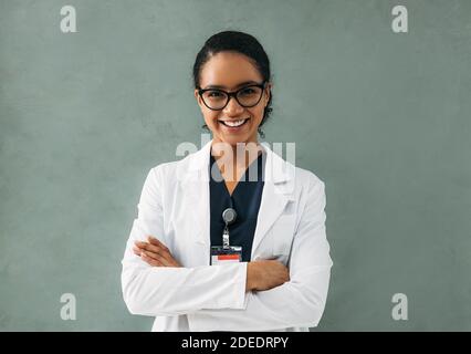 Porträt einer lächelnden Ärztin mit gekreuzten Armen. Junge Fachärztin mit Brille und weißer Jacke. Stockfoto