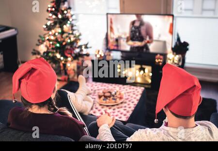Ein Paar schaut zu Weihnachten fern. Glücklicher Familienurlaub zu Hause. Mann und Frau auf der Couch entspannen mit Baum, Dekorationen, Lichter, Kerzen und Fernsehen. Stockfoto