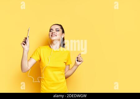 Fröhliche junge Frau, die mit Kopfhörern Musik hört und tanzt Genießen Sie Lieblingslieder auf gelbem Hintergrund Stockfoto