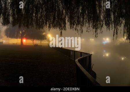 Ein stimmungsvoller Pfad entlang eines Flusses. In einer nebligen Winternacht in einer Stadt. Stockfoto